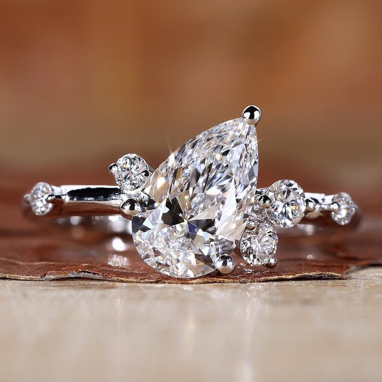 Elegant pear cut engagement ring with round side stones and basket setting, made of white gold.