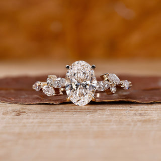 Side stone engagement ring with oval diamond and marquise accents in yellow gold.