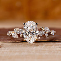 Side stone engagement ring with oval diamond and marquise accents in yellow gold.