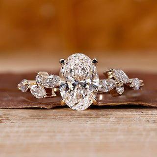 Side stone engagement ring with oval diamond and marquise accents in yellow gold.