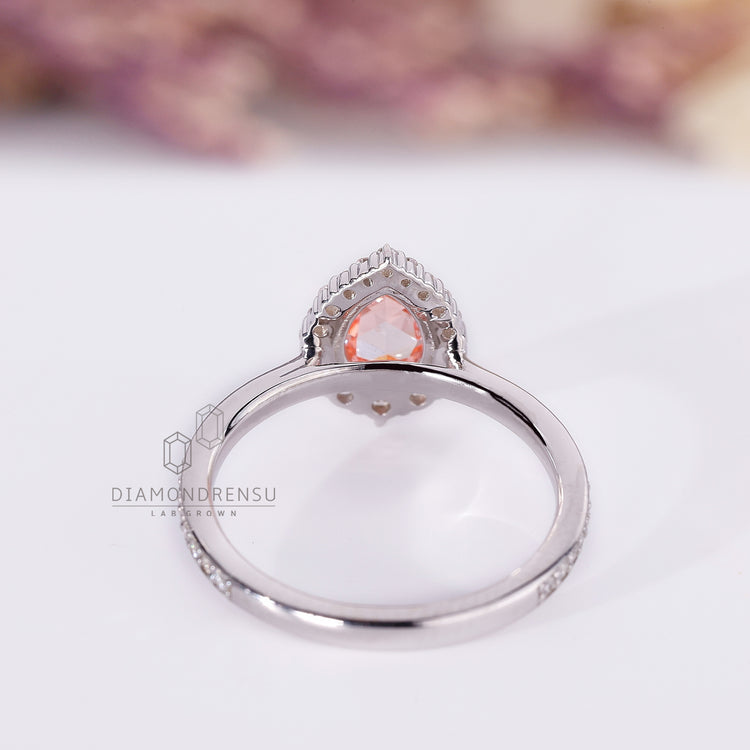 White gold ring with pink pear diamond and round halo stones.