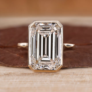 Bezel set emerald cut diamond ring with solitaire design.