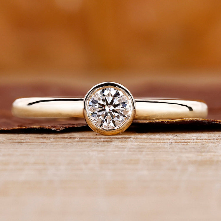 Round cut diamond ring in yellow gold with bezel setting.