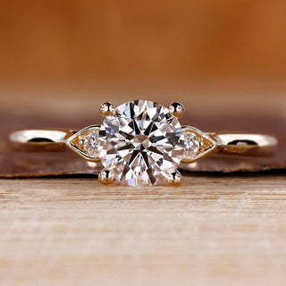 Round diamond ring in three stone style with pear shape outline.