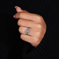 Emerald halo ring with round pave emeralds and radiant cut diamond centre in white gold.
