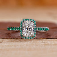 Radiant cut diamond ring with round cut emerald and claw prong setting in white gold.
