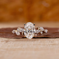 Side stone engagement ring with oval diamond and marquise accents in yellow gold.
