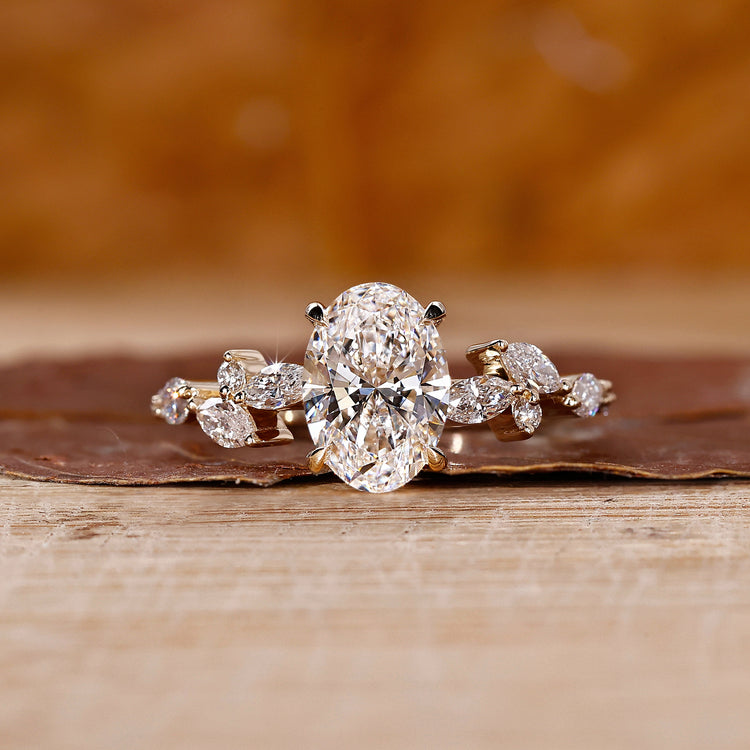 Side stone engagement ring with oval diamond and marquise accents in yellow gold.
