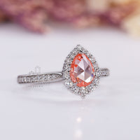 Round diamond halo ring with pink pear diamond and pavé details.
