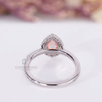 White gold ring with pink pear diamond and round halo stones.
