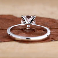 Cushion cut ring with a pave diamond band displayed on a velvet cushion.