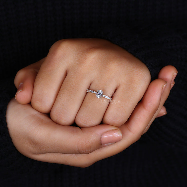 Side stone diamond ring with oval centre and 4-prong mount.
