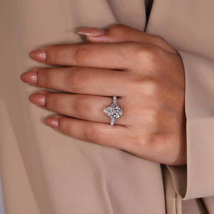 Round side stone ring with pear cut diamond in white gold.
