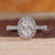 Elongated cushion cut diamond ring with round diamond halo setting.
