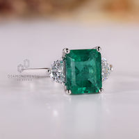 Emerald gemstone ring half moon side stones prong set.
