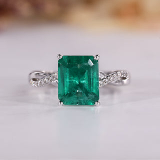 Emerald cut diamond ring with emerald gemstone and round diamond pave.
