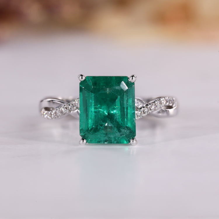 Emerald cut diamond ring with emerald gemstone and round diamond pave.
