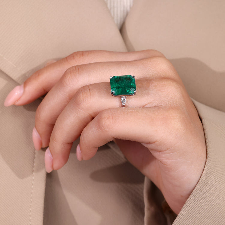 Emerald gemstone ring four prong distance pave style.
