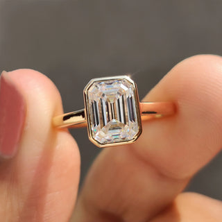 Bezel set engagement ring with Emerald cut diamond in yellow gold.