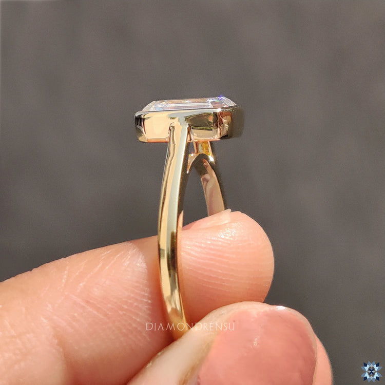 Bezel set engagement ring, featuring a Emerald cut diamond in yellow gold.