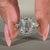 Emerald diamond ring in muse setting with side stones in white gold.
