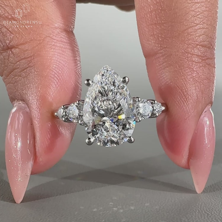 Pear and round diamond ring crafted with round side stones in a prong setting.
